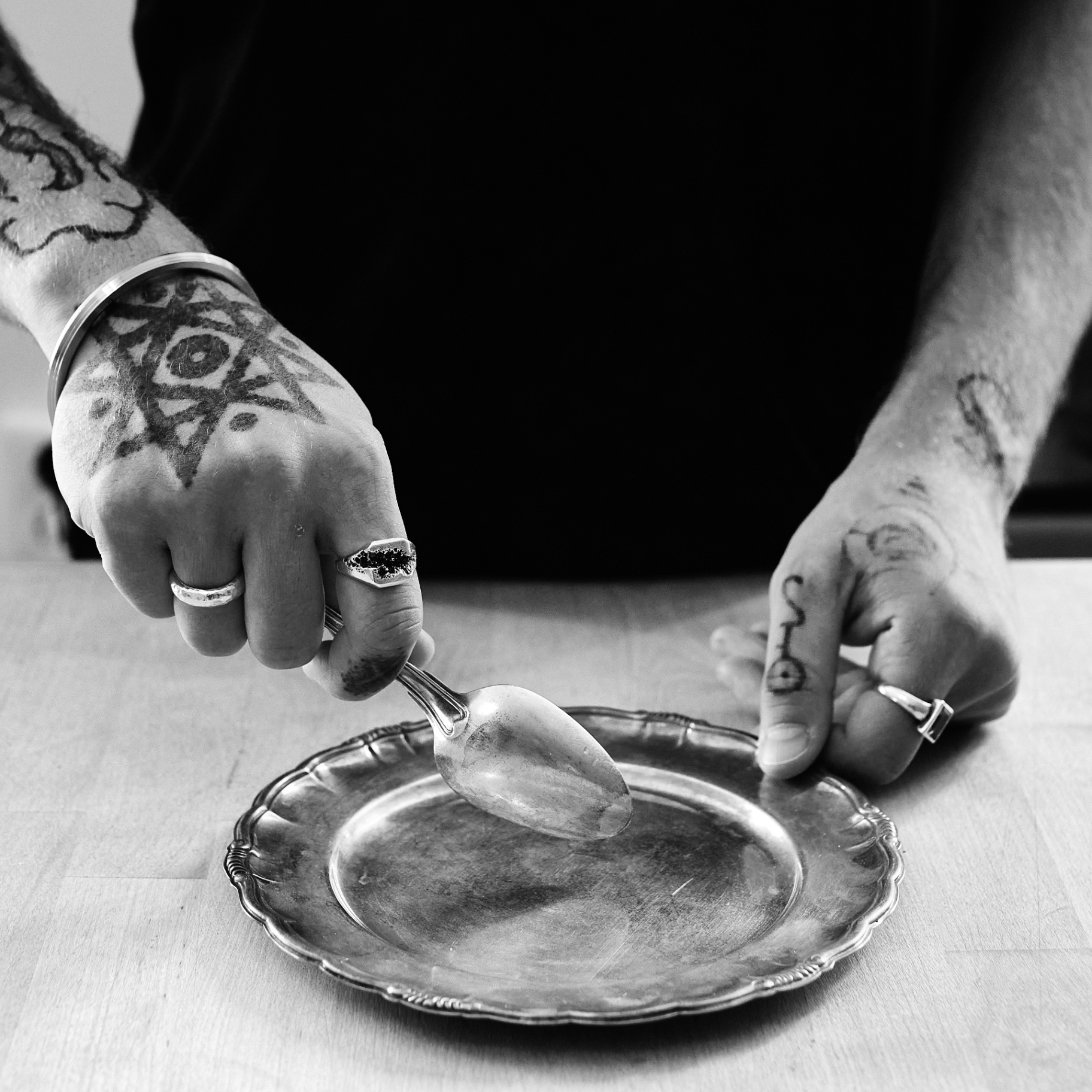 Tatuerade händer, en sked och ett silverfat, svartvitt